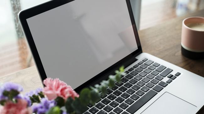 Bild på en laptop med en kopp kaffe bredvid och färska blommor